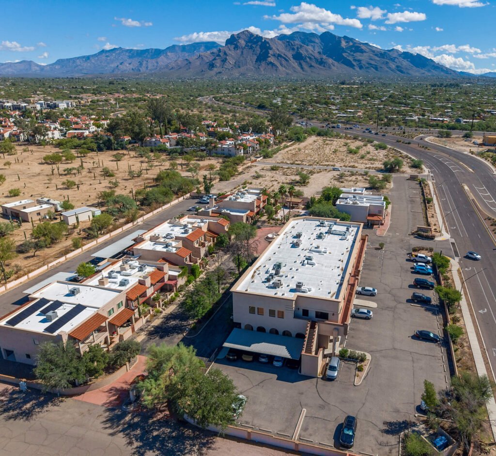 High-angle aerial drone shot of a commercial complex and parking lot in Tucson with the Santa Catalina Mountains in the background.